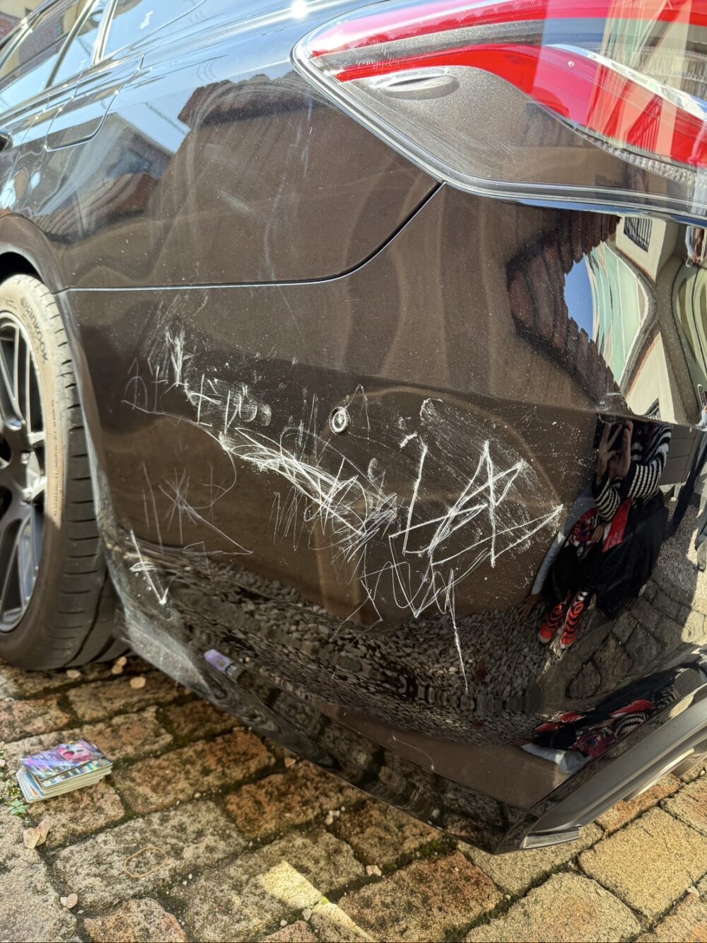 黒い車に、小石で思い切り落書き。キズだらけの車